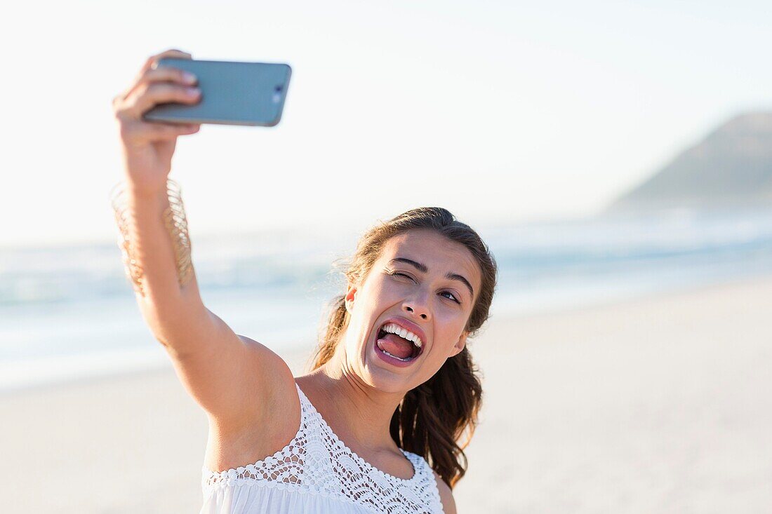 Playful young woman taking selfie with smartphone on the beach
