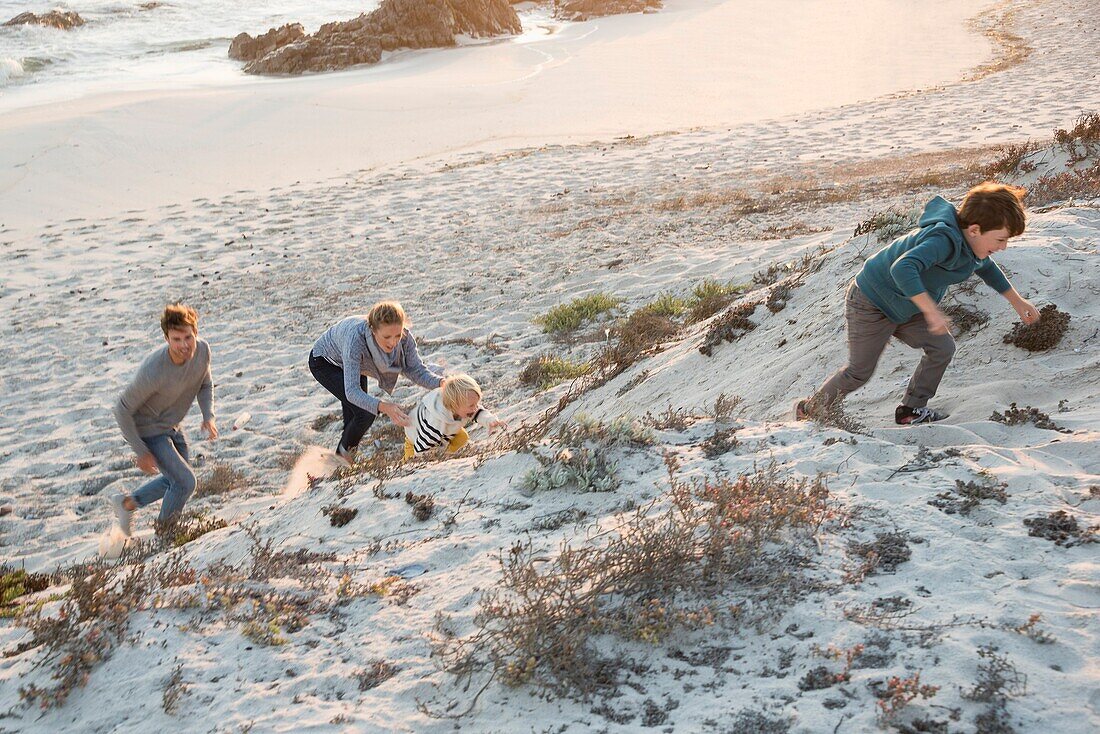 Happy young family climbing sand dune on beach at sunset