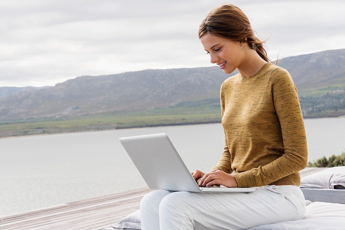 Hübsche junge Frau benutzt einen Laptop am Seeufer