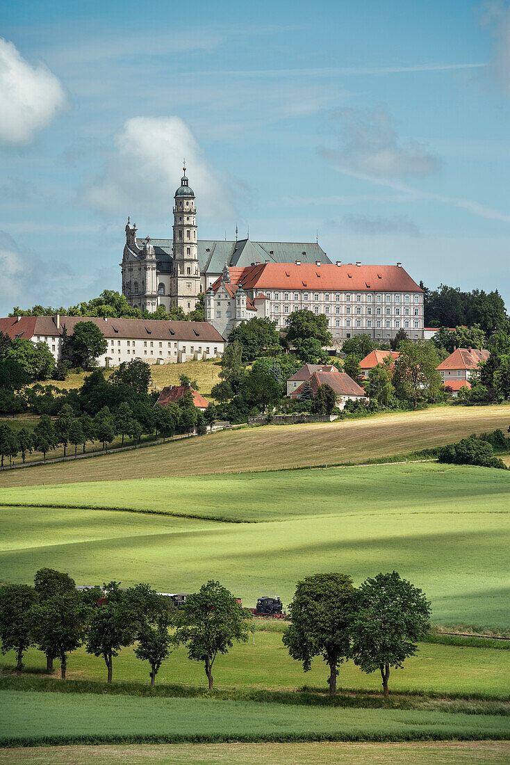 historical steam train passes Benedictine abbey at the so called Haertsfeld, Neresheim monastry, Ostalb district, Swabian Alb, Baden-Wuerttemberg, Germany