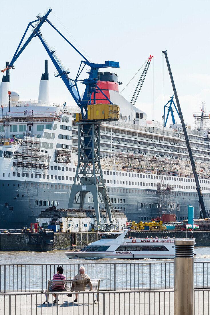 A pair sitting at the landing stages in front of the dry dock of the shipyard Blohm and Voss where the cruise ship QE2 is being overhault, Hamburg, Germany