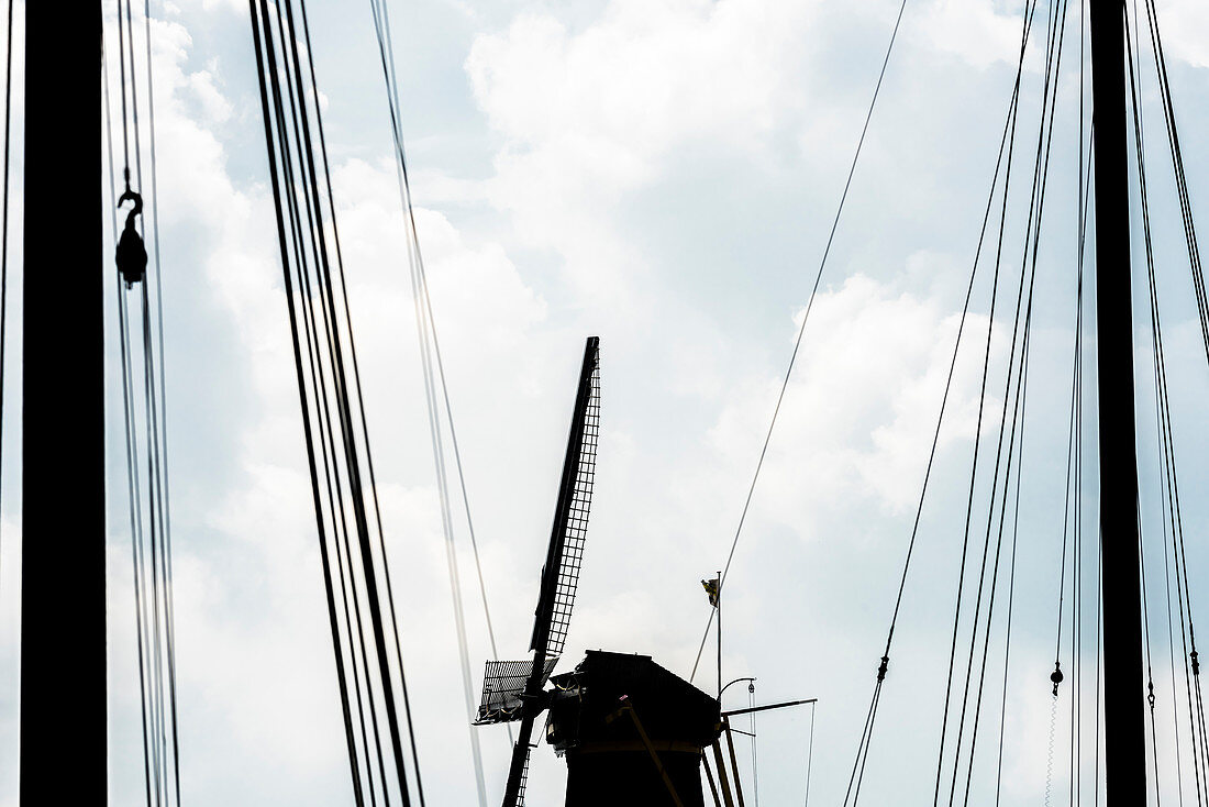 Die Silhouette einer Windmühle am Delfshaven eingerahmt von der Takelage eines alten Segelschiffes, Rotterdam, Provinz Südholland, Niederlande