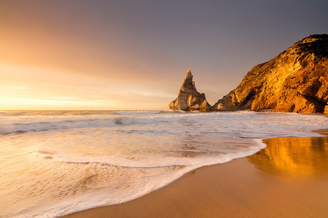 Golden reflections of the cliffs on Praia da Ursa beach bathed by ocean at sunset, Cabo da Roca, Colares, Sintra, Portugal, Europe