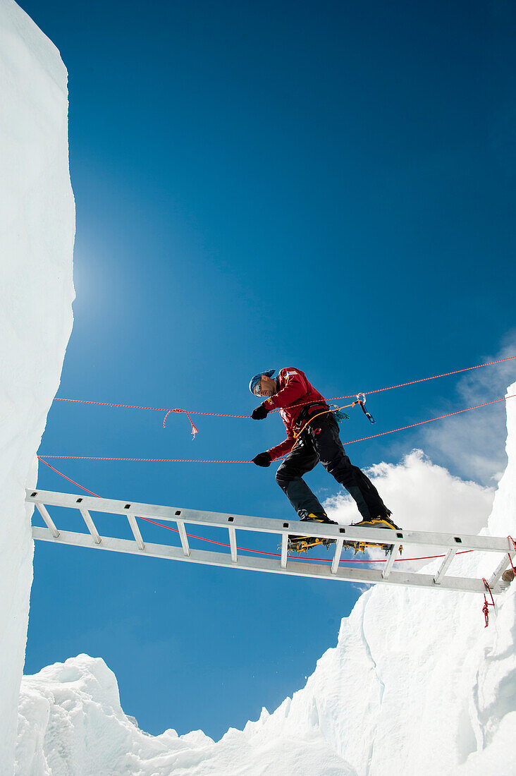 A climber makes his way across a crevasse using a temporary ladder, Khumbu region, Himalayas, Nepal, Asia