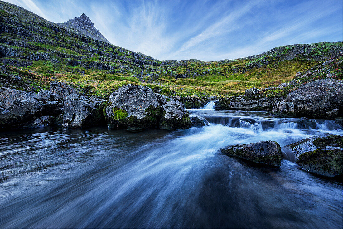 'A mountain stream runs toward the ocean in the fjord called Mjoifjordur, East Iceland; Iceland'