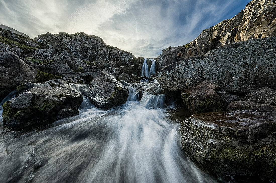 'Stream flows over a waterfall and through the rocks along the eastern coast of Iceland; Iceland'
