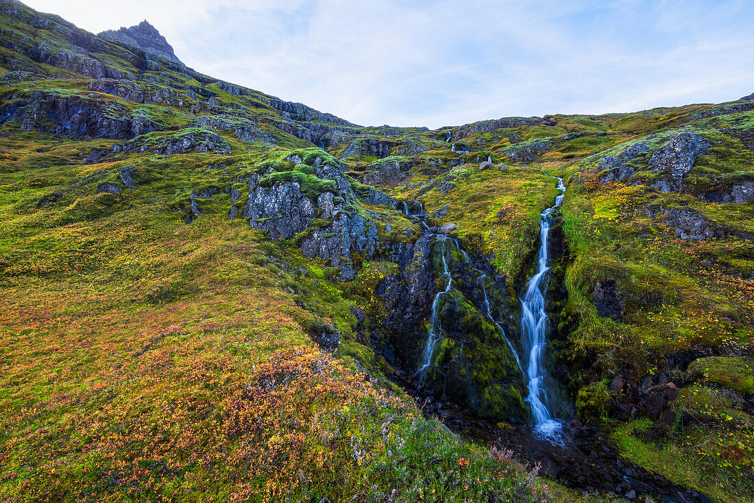 'A small waterfall tumbles down the mountain side in one of Iceland eastern fjords; Iceland'