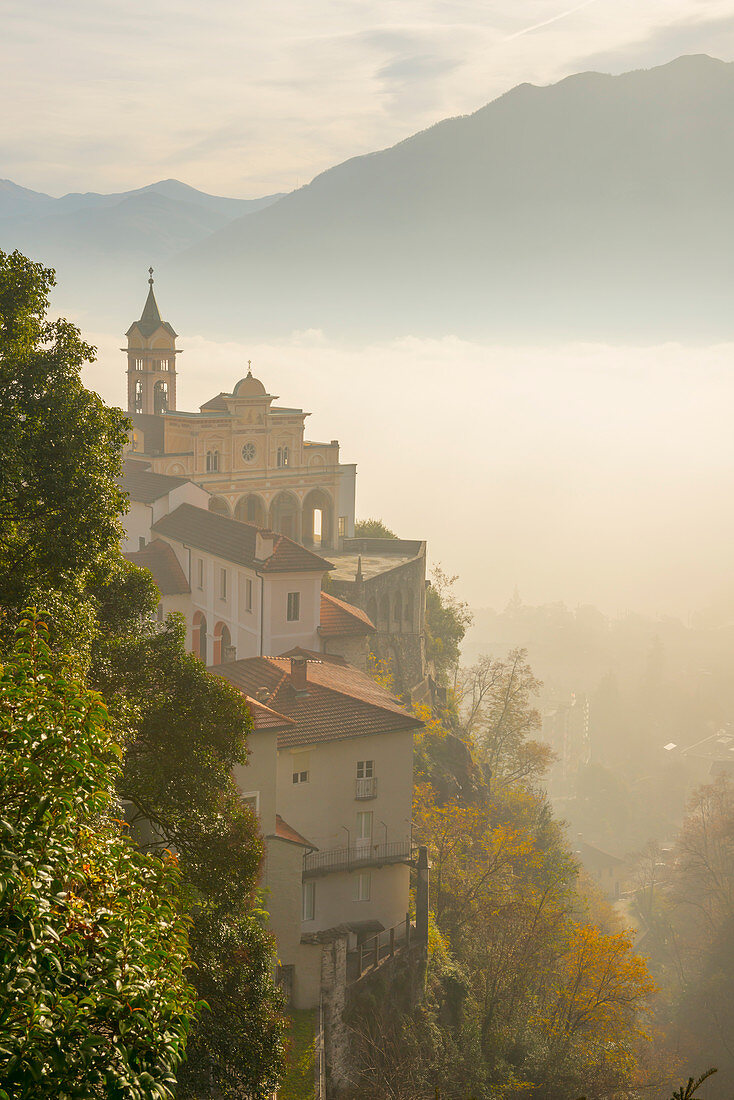 'Fog sets in over a church and alpine lake; Locarno, Ticino, Switzerland'