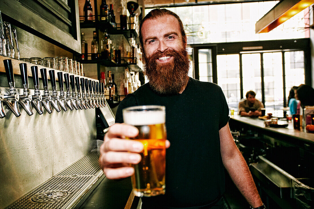 Smiling Caucasian bartender serving beer at bar