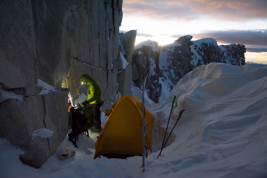 A man camped on the summit ridge after  climbing Thunderbolt Ridge in Hogum Fork while on a backcountry ski tour in Little Cottonwood Canyon, Lone Peak Wilderness, Uinta-Wasatch-Cache National Forest, Salt Lake City, Utah.