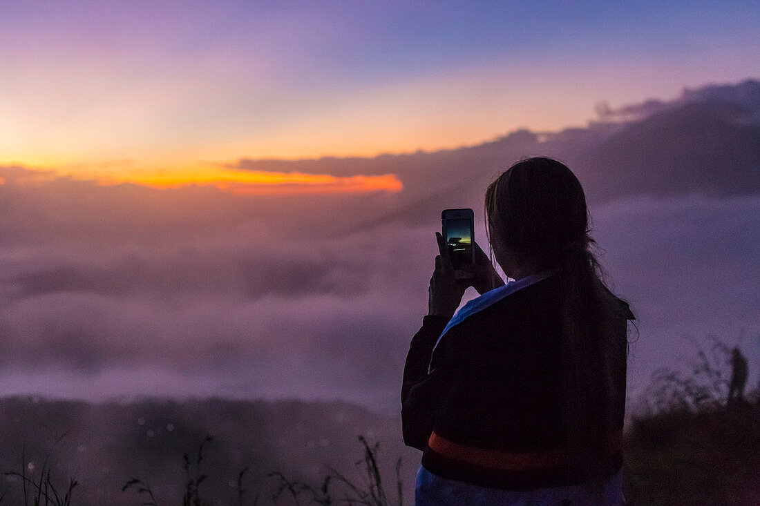 Female takes photos with smartphone in mountains at sunrise