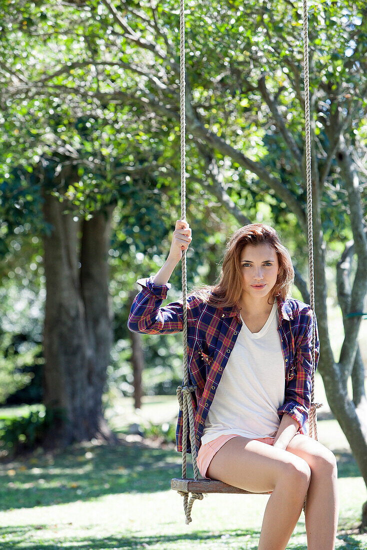 Young woman sitting on swing in park, portrait