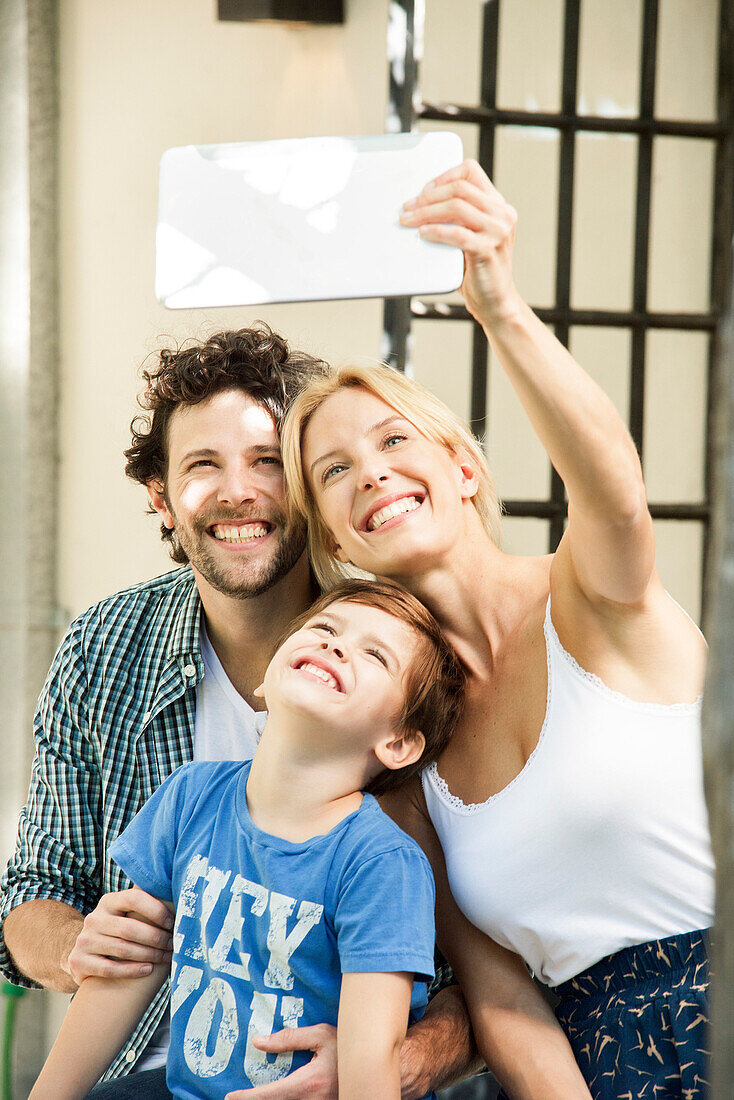 Family with one child posing for selfie taken with digital tablet