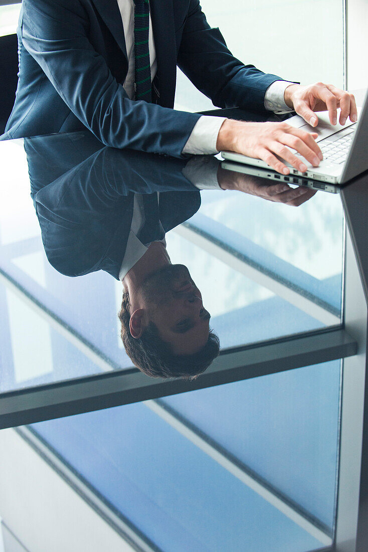 Businessman using laptop computer, reflection on glass top table