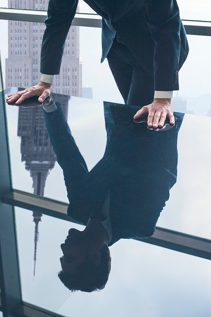 Businessman leaning against table, reflection in glass top