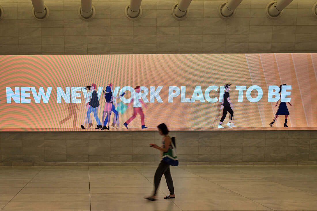 woman passing a lit advertisement in a corridor of the Oculus while looking at her mobile phone, futuristic train station by famous architect Santiago Calatrava next to WTC Memorial, Manhattan, New York City, USA, United States of America