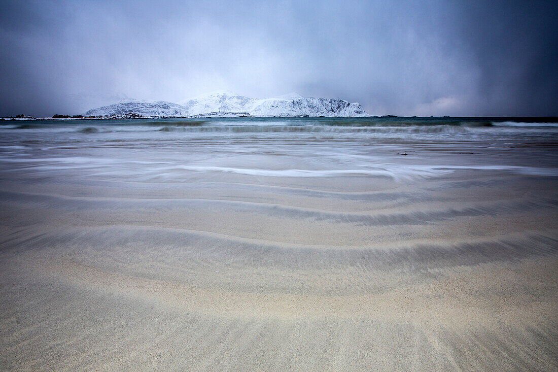 Waves of the icy sea on the beach in the background the snowy peaks Ramberg Lofoten Islands Norway Europe