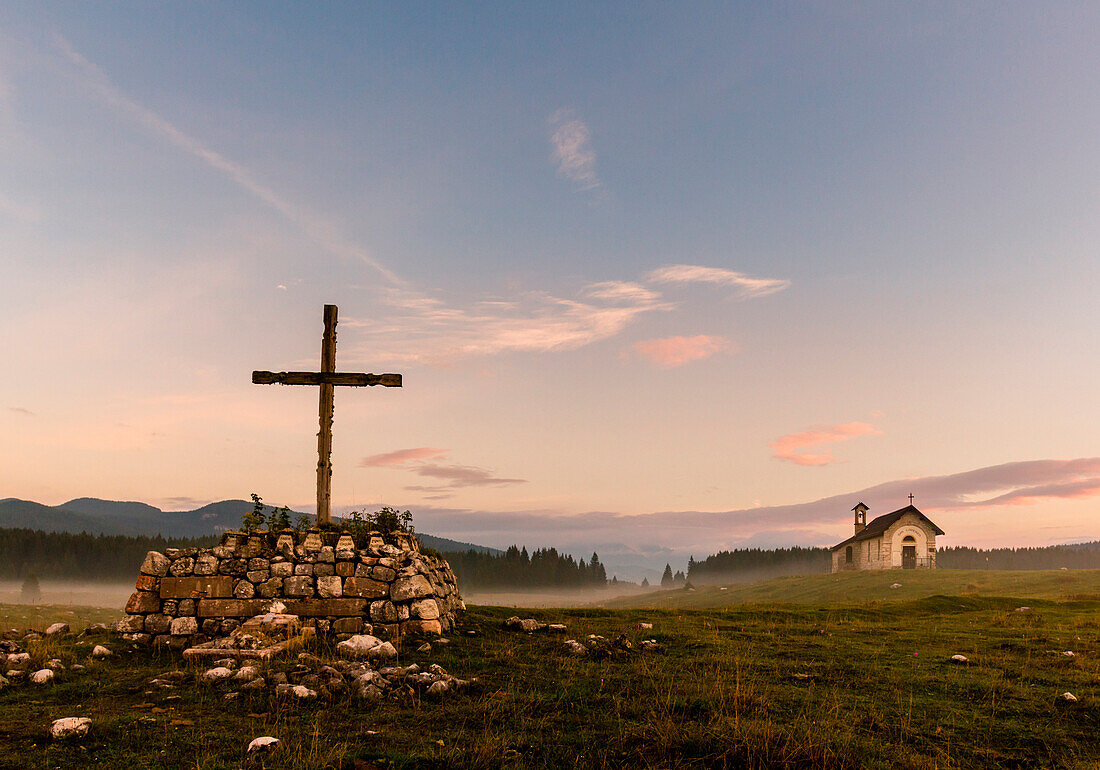 Wooden Cross, Plains of Marcesina, Altopiano of Asiago, Province of Vicenza, Veneto, Italy. Saint Lorenzo church in the mist.