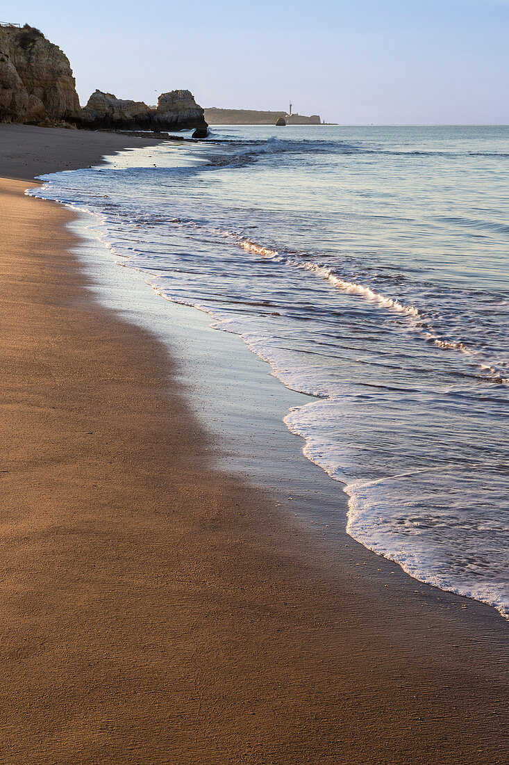 The rising sun illuminates the fine sand bathed by the blue ocean Praia do Vau Portimao Faro district Algarve Portugal Europe