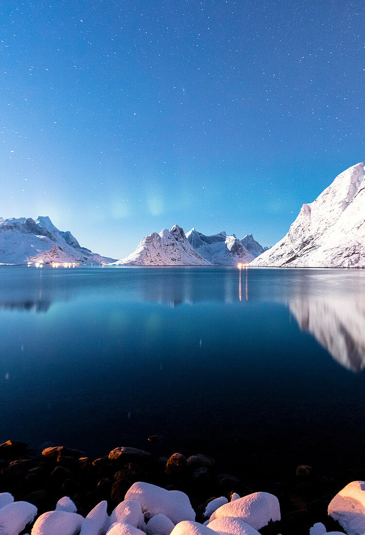 The snowy peaks are reflected in the frozen sea on a starry winter night Reine Bay Nordland Lofoten Islands Norway Europe