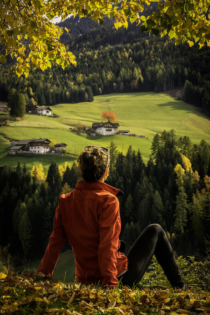 Girl sitting on the filed admiring the view of the Val di Funes, Trentino Alto Adige, Italy.