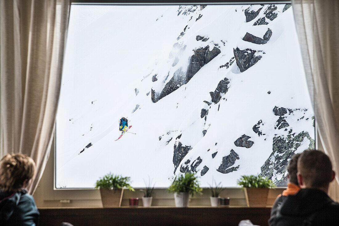 Gäste beobachten einen Skifahrer bei einem Sprung durchs Fenster, Andermatt, Uri, Schweiz