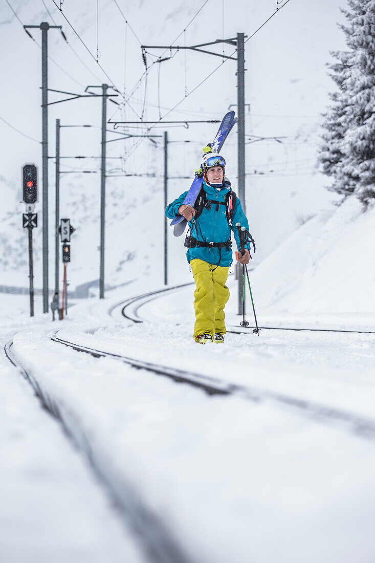 Junger Skifahrer läuft eine verschneite Eisenbahnschiene entlang, Andermatt, Uri, Schweiz