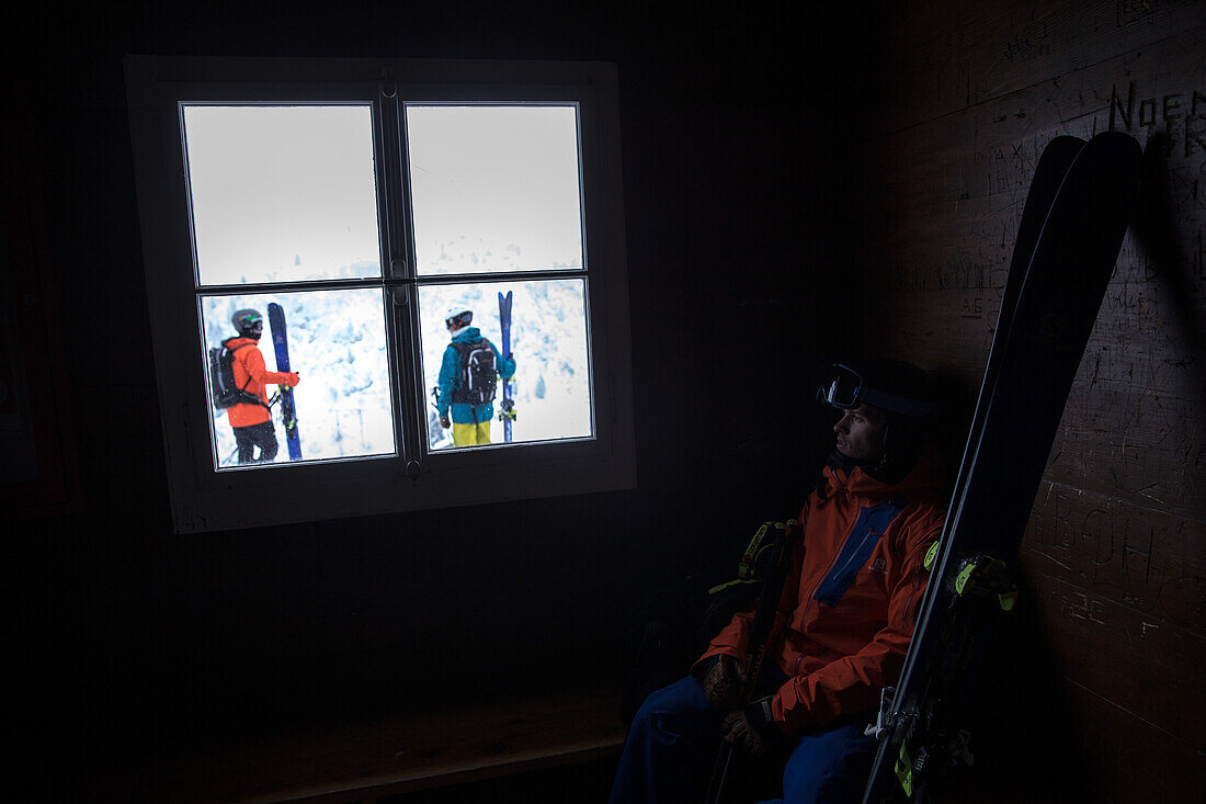 Young male skier looking at at other skiers through a window, Andermatt, Uri, Switzerland