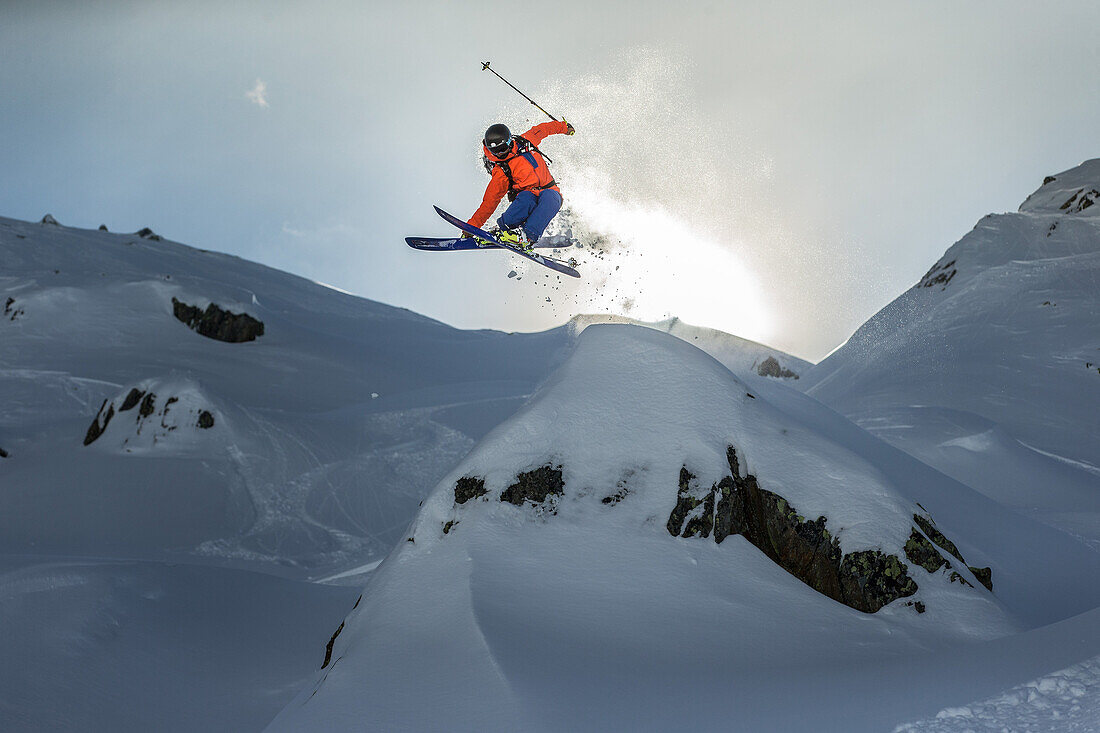 Junger Skifahrer springt über einen Felsten abseits der Pisten, Andermatt, Uri, Schweiz