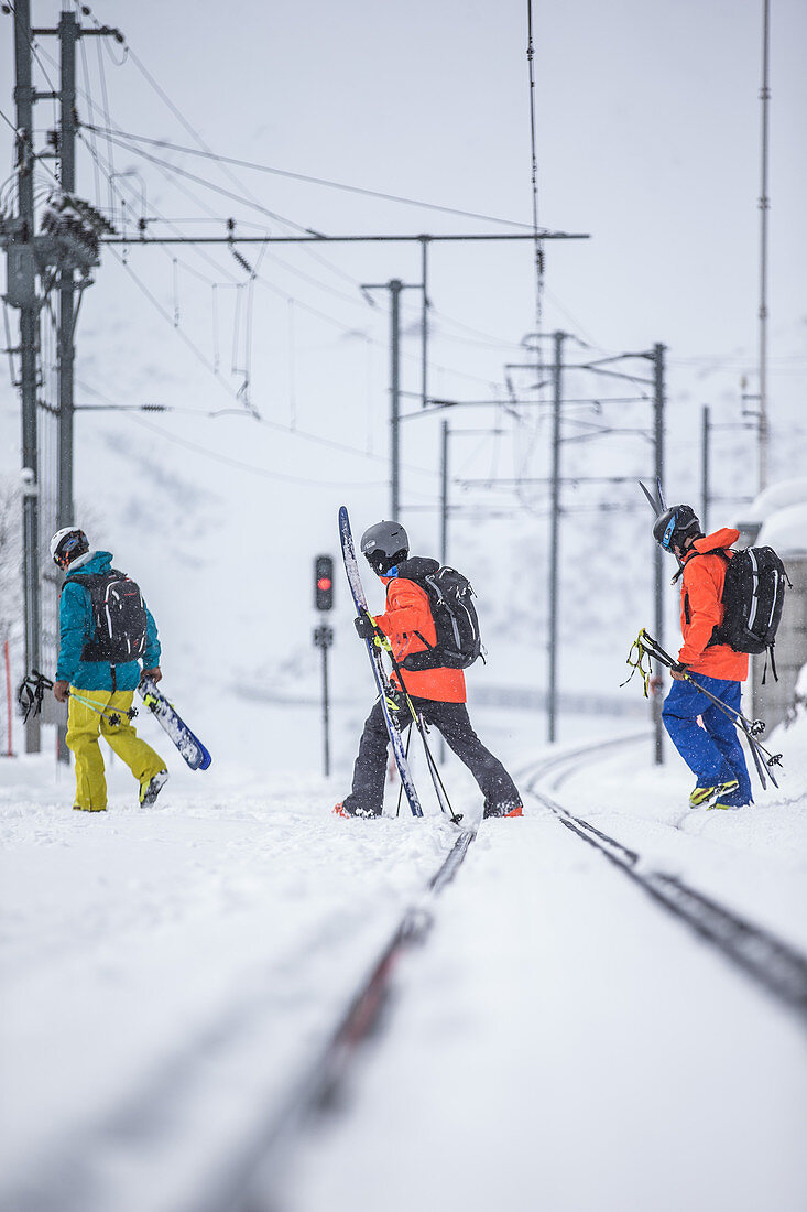 Drei junge Skifahrer gehen über Eisenbahnschienen, Andermatt, Uri, Schweiz