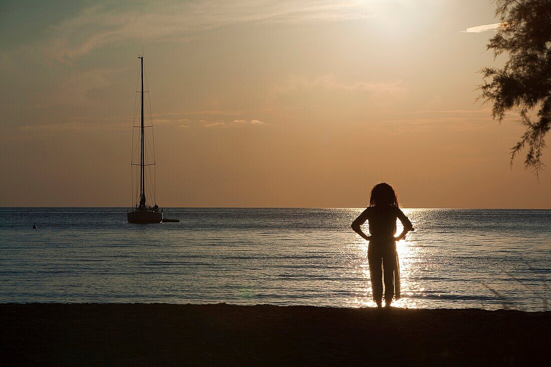 Silhouette of a woman standing on the beach near the port in Kamares at sunset, Sifnos, Cyclades Islands, Greek Islands, Greece, Europe.