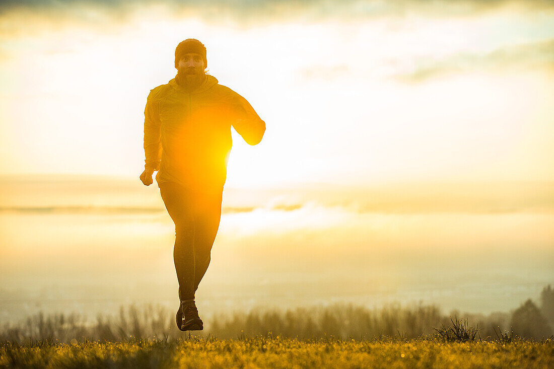 Young man running over a meadow during sunset, Allgaeu, Bavaria, Germany