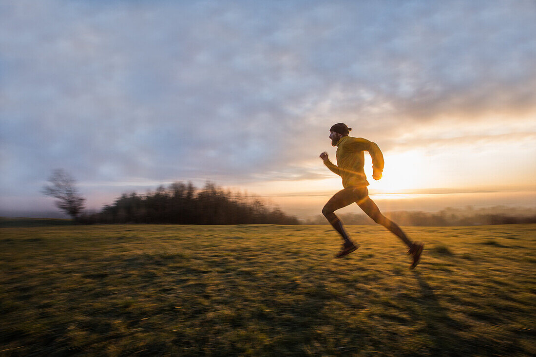 Young man running over a meadow during sunrise, Allgaeu, Bavaria, Germany