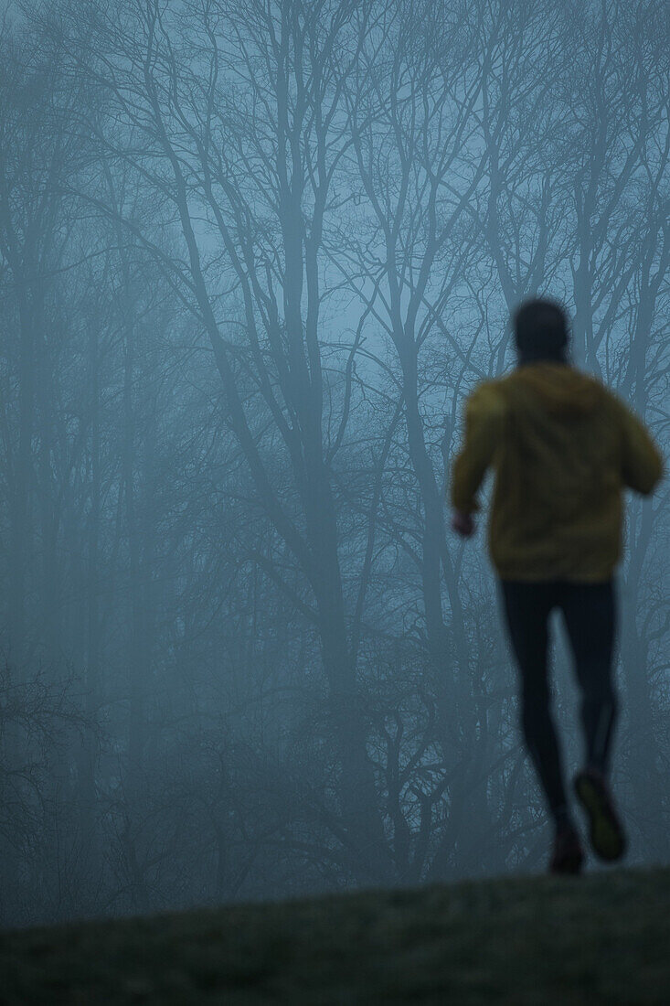 Young man running over a meadow on a foggy autumn day, Allgaeu, Bavaria, Germany