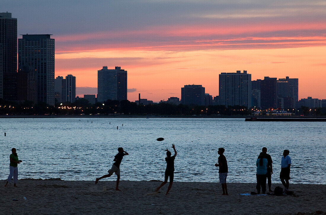 USA, Illinois, Chicago, Gold Coast und Gebäude am Rande des Lake Michigan im Sonnenuntergang von Olive Park Beach, Frisbee-Spieler