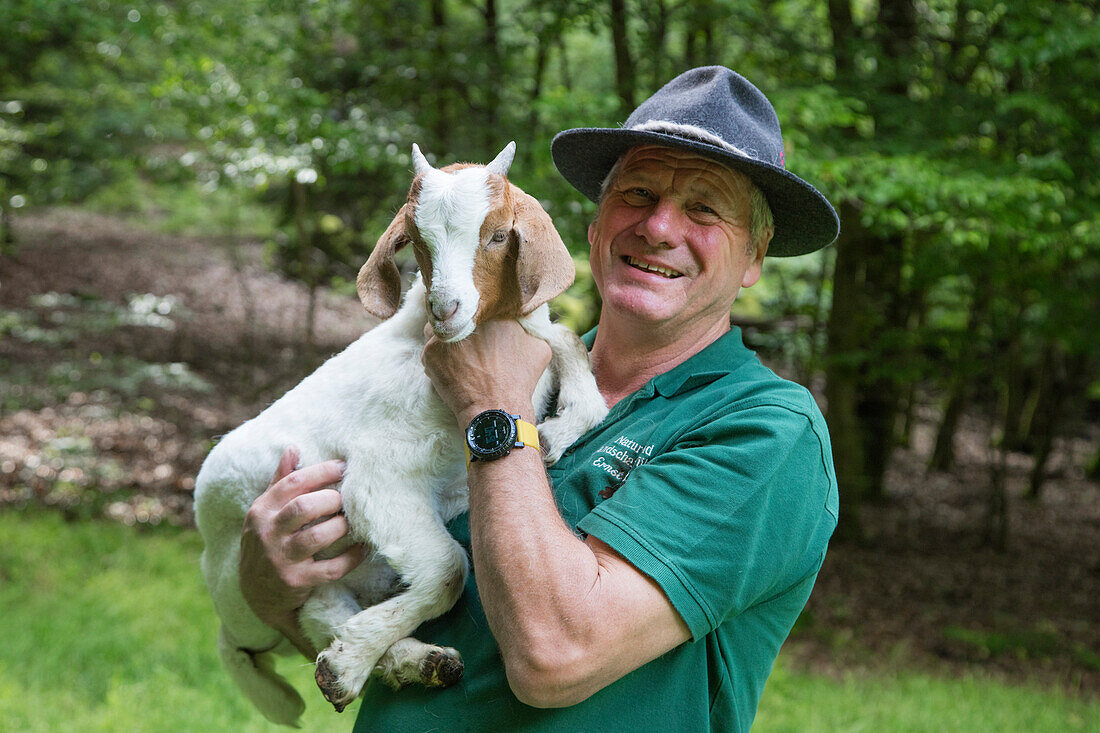 Natur- und Landschaftsführer Ernst mit junger Ziege auf dem Arm, nahe Mespelbrunn, Räuberland, Spessart-Mainland, Bayern, Deutschland