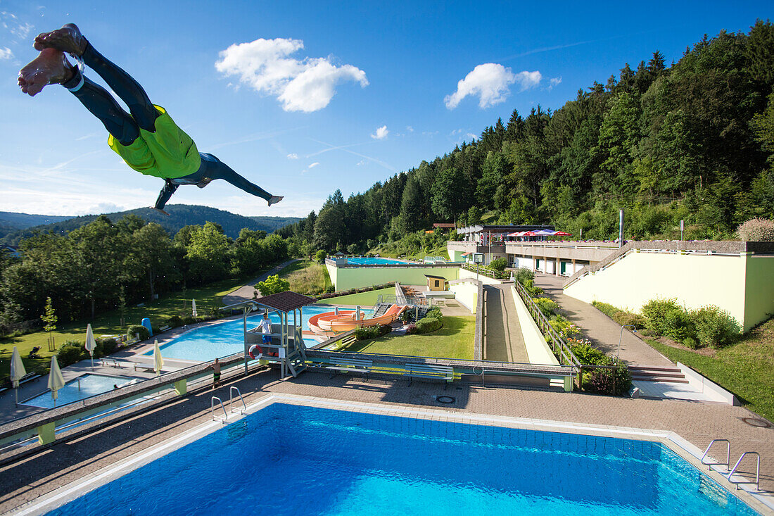 Young man jumps from 5 meter diving tower into swimming pool at Freibad Terrassenbad Frammersbach, Frammersbach, Spessart-Mainland, Bavaria, Germany