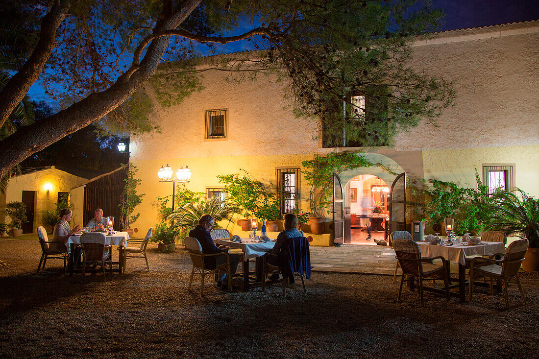 Gäste genießen ihr Abendessen draußen am Hof von Finca Predio Son Serra Hotel in der Abenddämmerung, nahe Muro, Mallorca, Balearen, Spanien