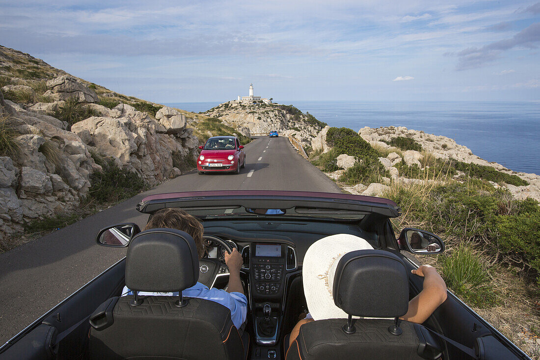 Paar in Sunny Cars Cabriolet auf Straße entlang der Halbinsel Cap de Formentor mit Leuchtturm Faro de Formentor im Hintergrund, Cap de Formentor, Mallorca, Balearen, Spanien