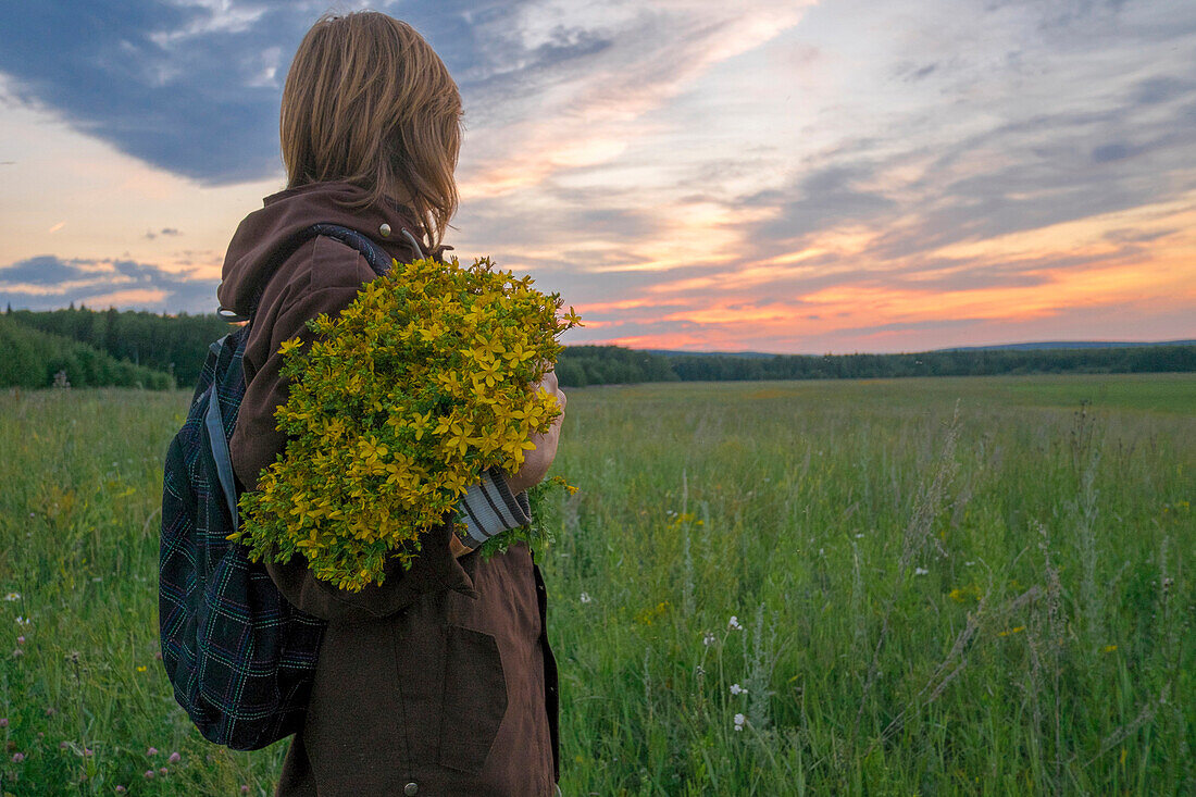 Caucasian woman holding bouquet of flowers in field at sunset