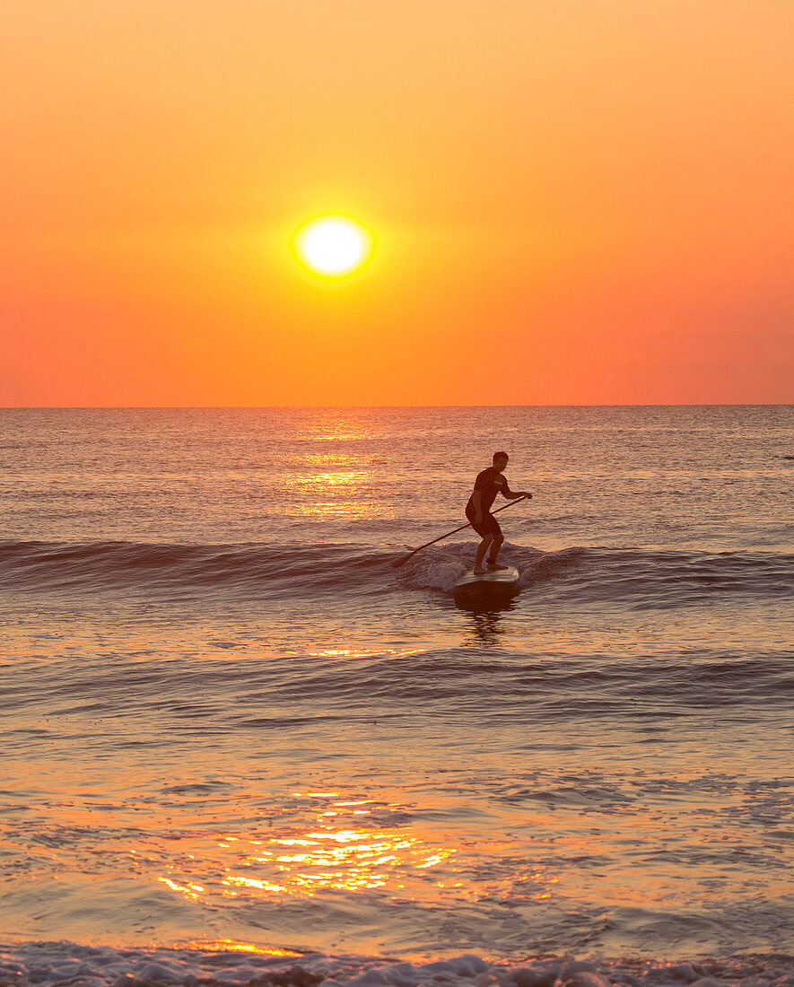 Silhouette of man paddleboarding on ocean waves
