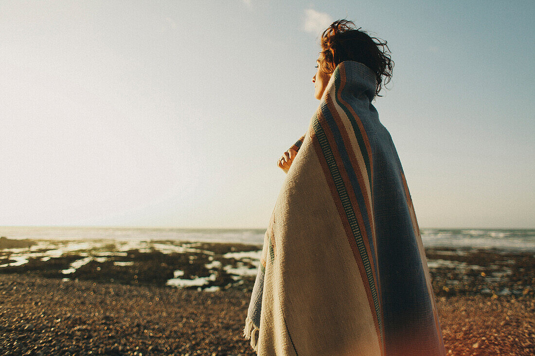 Caucasian woman wrapped in blanket at beach