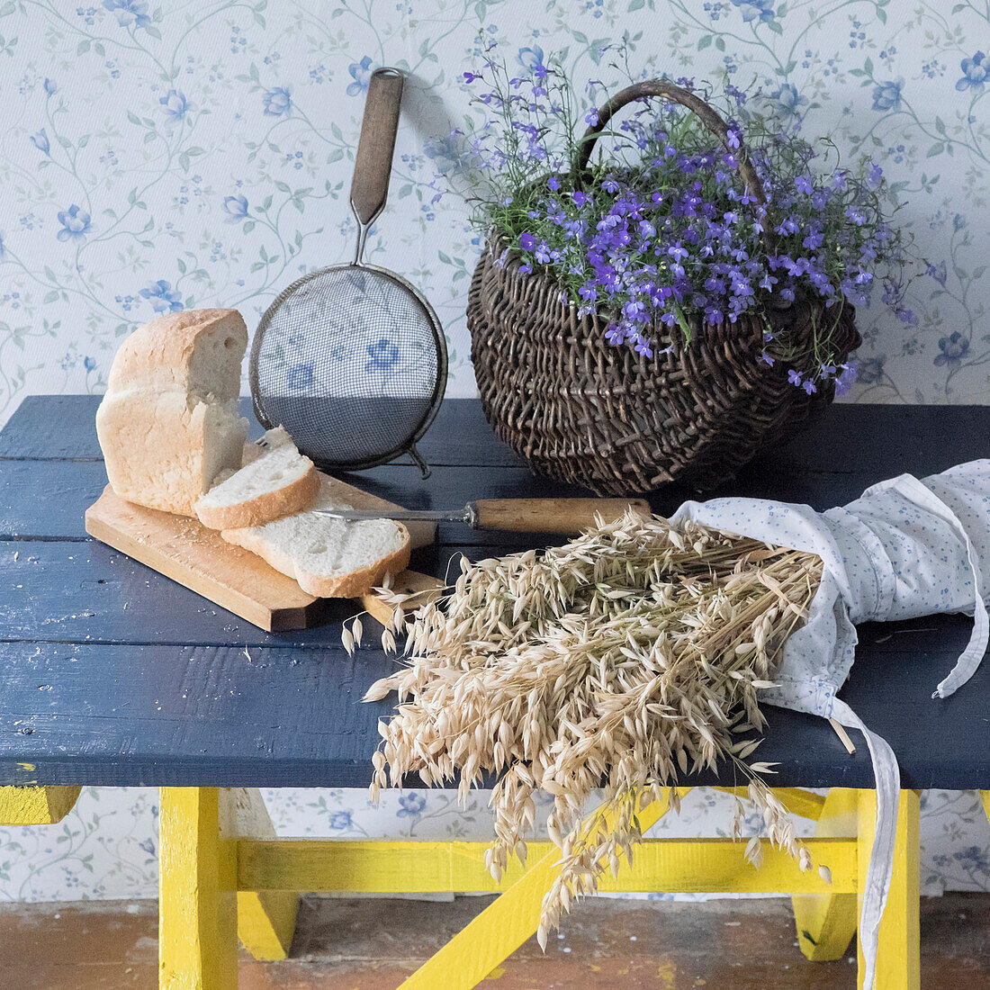 Wheat, sliced bread, sieve and flowers on bench