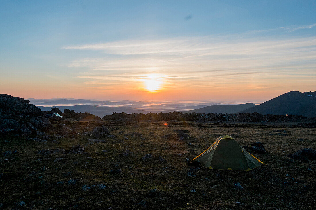 Camping tent in barren field at sunset