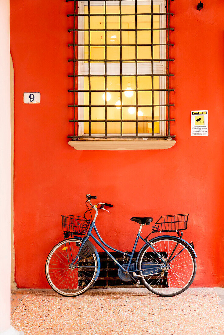 Blue bicycle leaning on orange wall under window