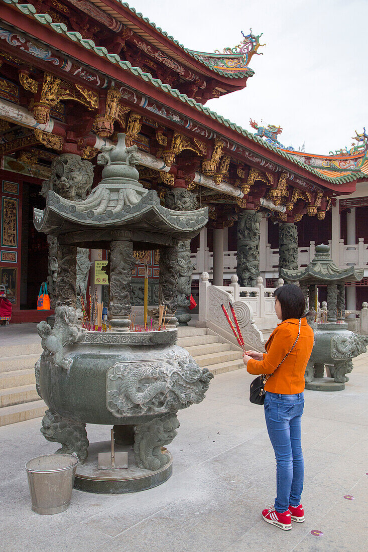 Frau hält Räucherstäbchen während des Gebets an einem Tempel im A-Ma Cultural Village, Coloane, Macau, China