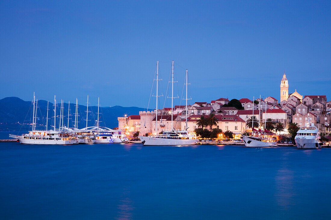 Motor sailing cruise ship M/S Panorama (Variety Cruises) and other yachts at pier with Korcula Old Town and St. Mark's Cathedral at dusk, Korcula, Dubrovnik-Neretva, Croatia