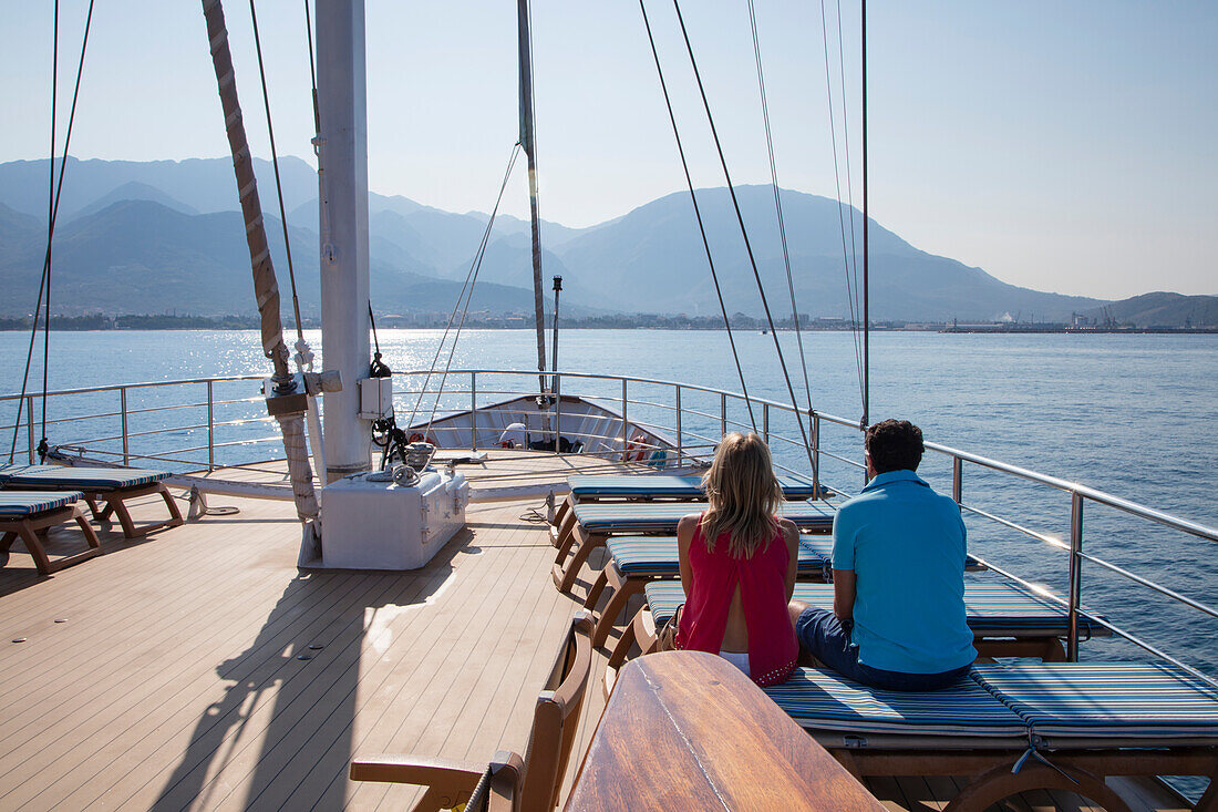 Couple on deck of motor sailing cruise ship M/S Panorama (Variety Cruises) on approach to harbor with mountain backdrop, near Bar, Montenegro