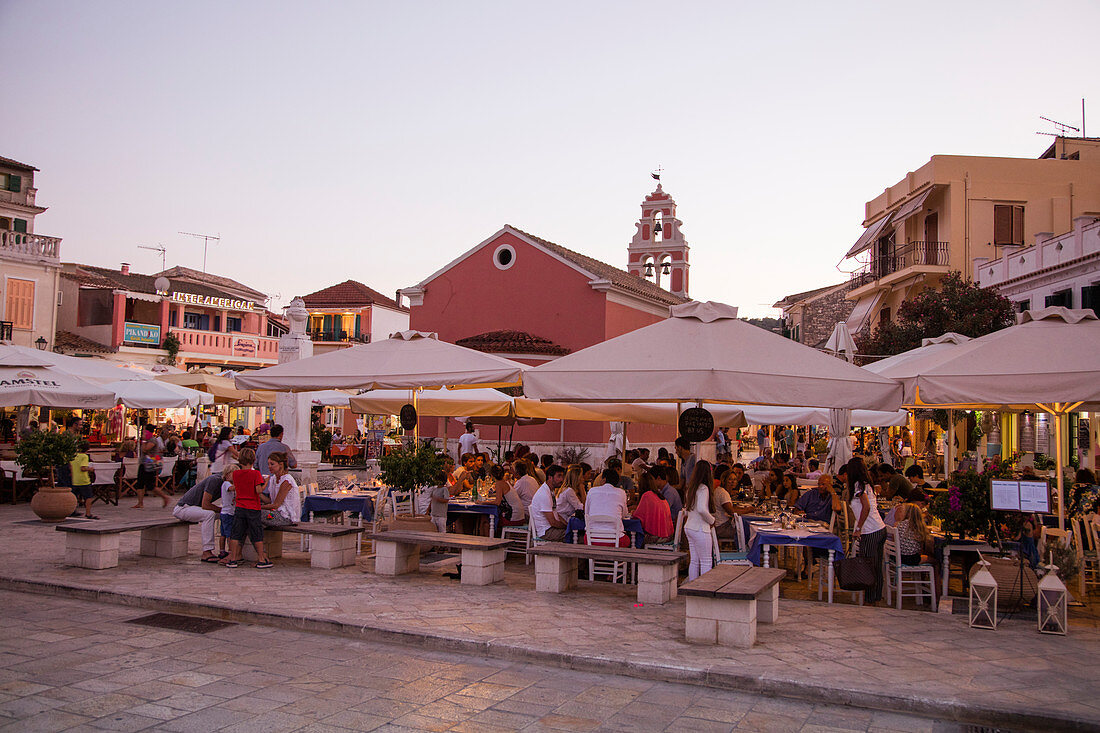Menschen sitzen draußen und genießen ihr Abendessen in einem Restaurant auf der Plaza bei Sonnenuntergang, Gaios, Paxos, Ionische Inseln, Griechenland