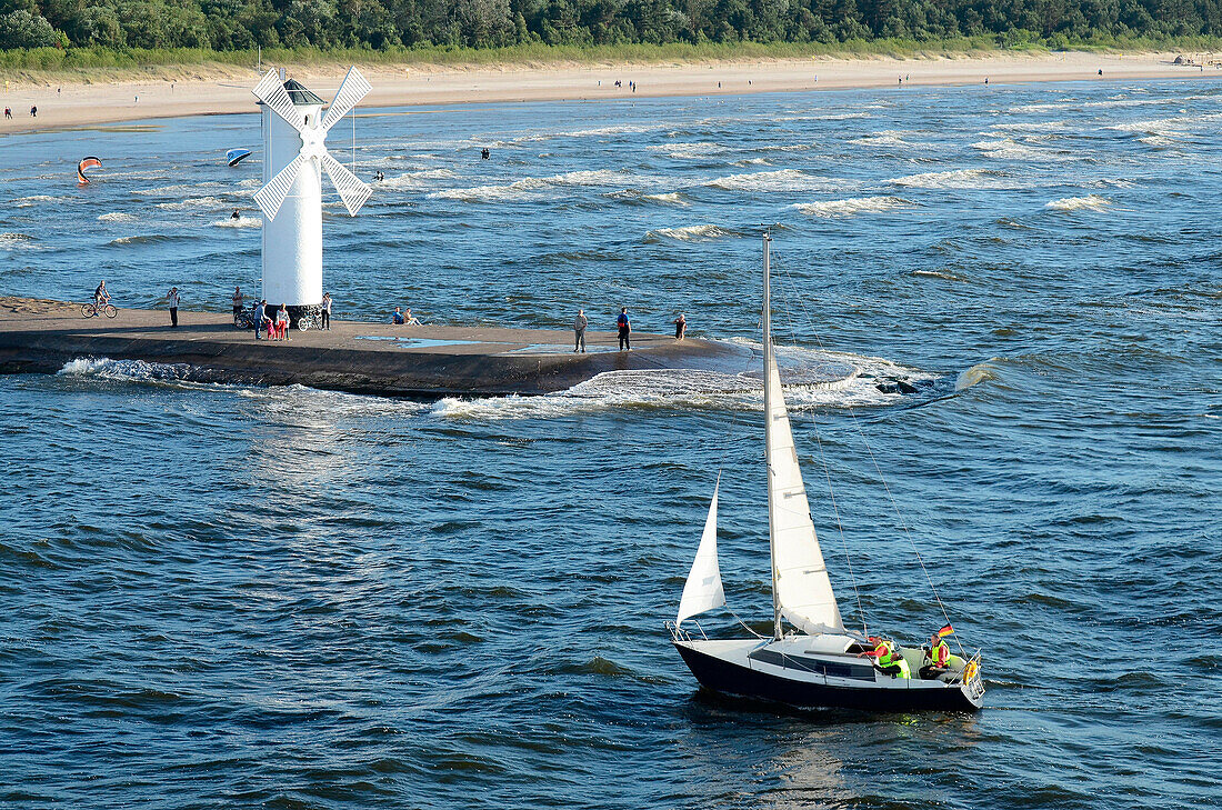 A sail boat passing the lighthouse at harbor in Swinoujscie, Poland